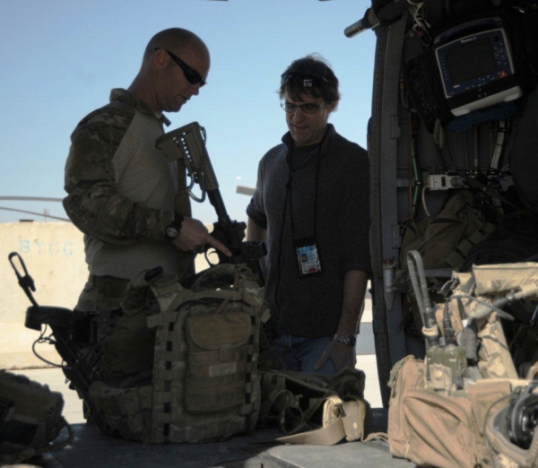 A pararescue soldier holding an M4 discusses gear with Phil Scott as the helicopter is loaded.